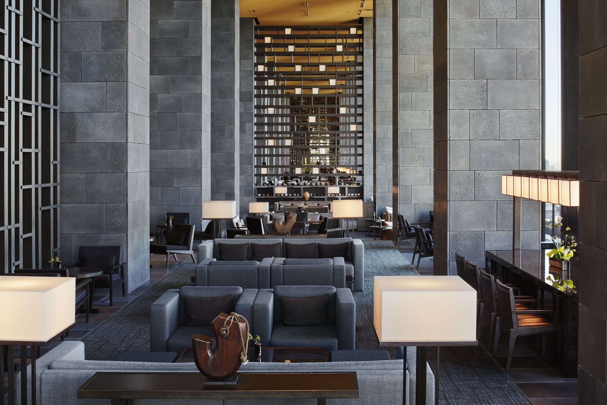 Aman Tokyo lounge with soaring stone walls, low seating and illuminated shelving