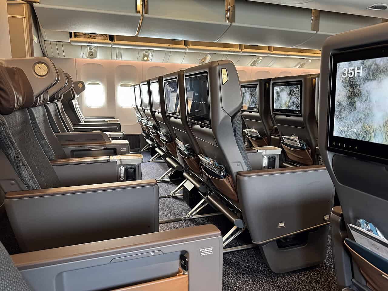 Rows of brown and taupe fixed-shell premium economy recliner seats with leg rests and large seatback screens aboard a Cathay Pacific Boeing 777-300ER, one screen showing seat number 35H