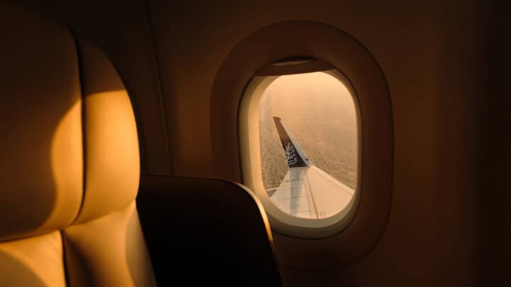 Warm golden light inside the Four Seasons Private Jet cabin, with a tan leather seat beside an oval window looking out over the wing and its Four Seasons tree logo on the winglet
