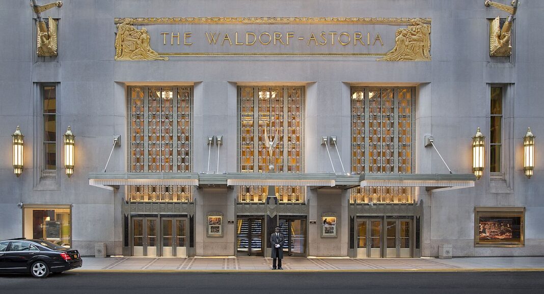 Hilton Diamond Benefits: What You Actually Get and the Fastest Way In Art Deco limestone facade of the Waldorf Astoria New York with gilded relief panels, gold lettering reading THE WALDORF-ASTORIA, lit lanterns and a uniformed doorman under the Park Avenue canopy