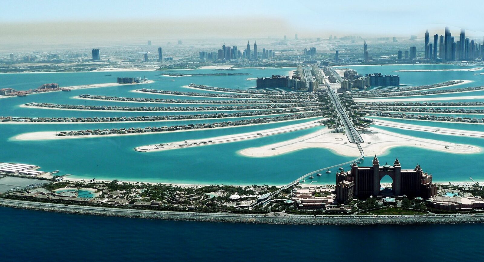 Aerial view of Palm Jumeirah in Dubai, with the palm-frond residential islands in turquoise water, the arch-shaped Atlantis The Palm hotel on the outer crescent in the foreground and the Dubai Marina skyline on the hazy horizon